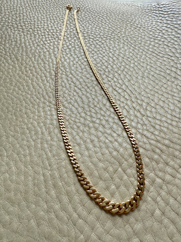 Gold chain necklace on a textured beige surface