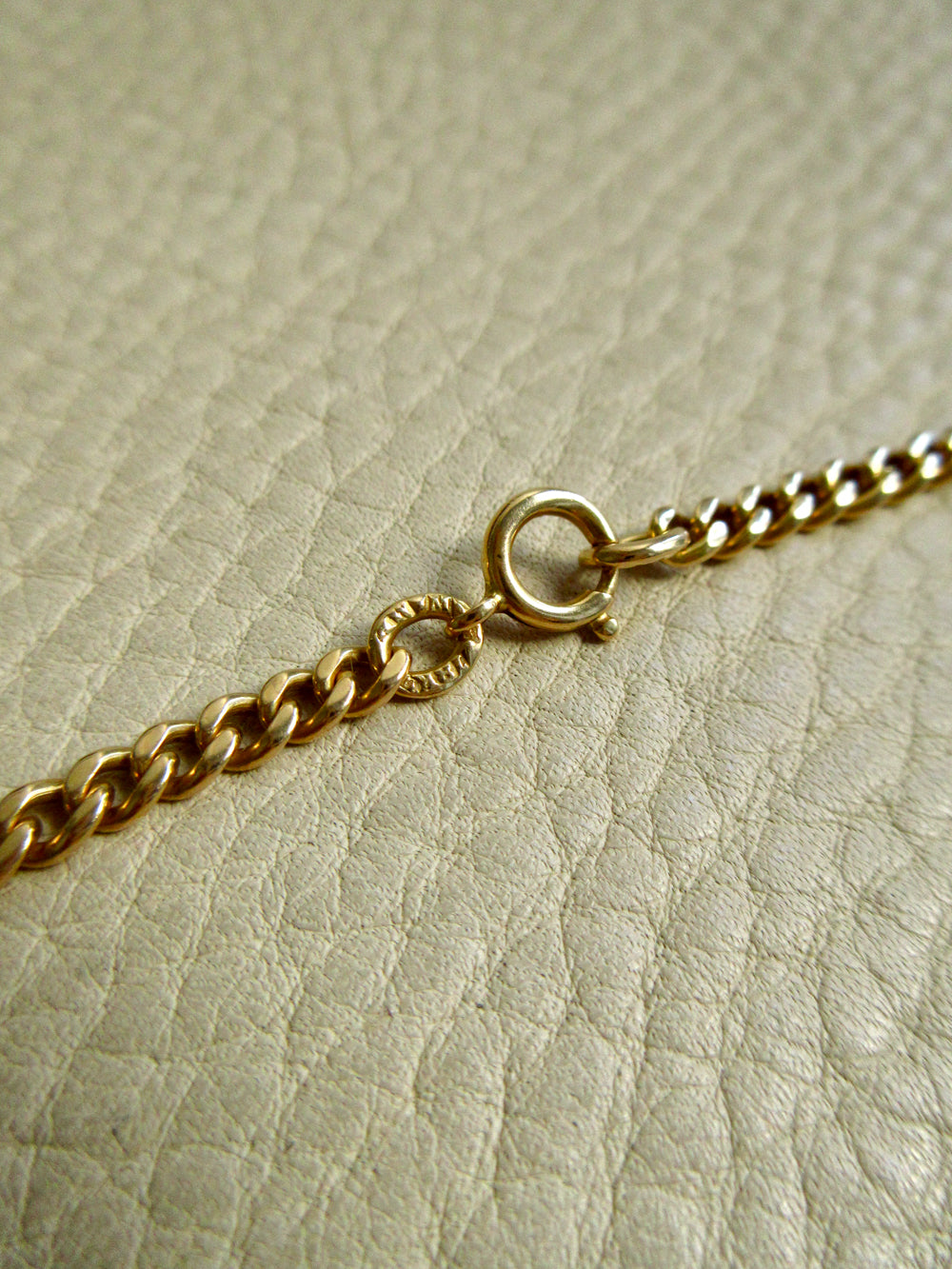 Close-up of a gold chain with a spring clasp resting on a textured beige leather surface.