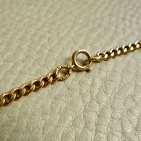 Close-up of a gold chain with a spring clasp resting on a textured beige leather surface.
