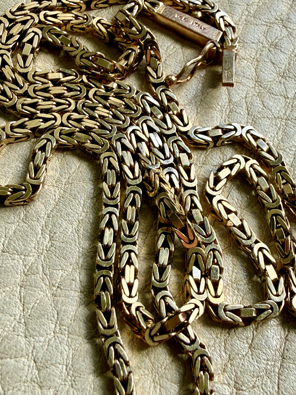 14k gold Gold byzantine chain necklace on a textured beige surface penelopepenelope.com fine jewelry