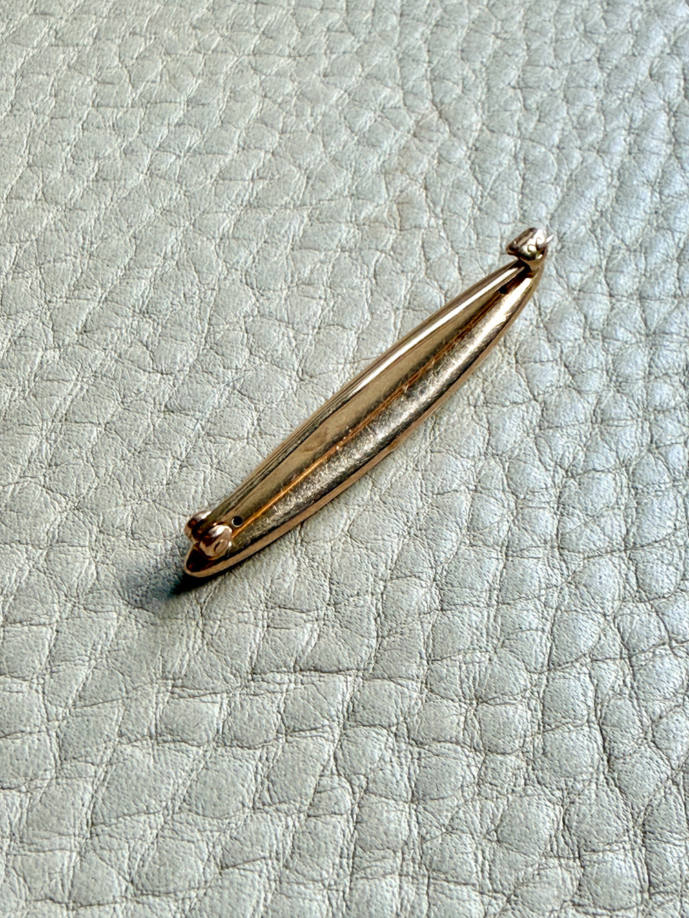14k Gold brooch on a textured light blue surface