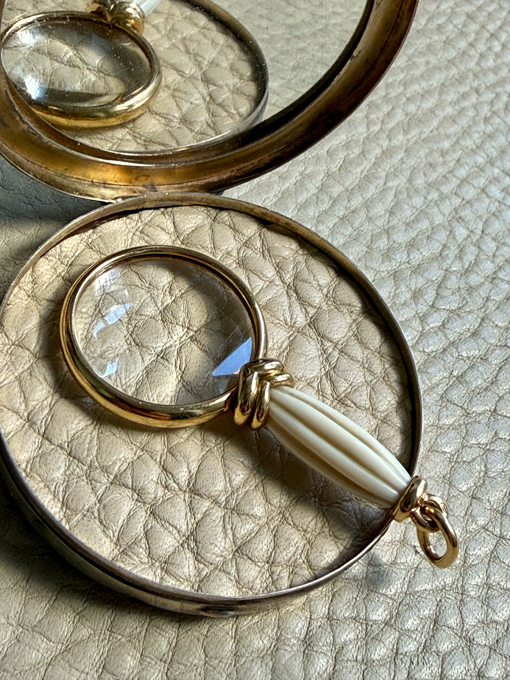 18k gold quizzing glass magnifying glass pendant on a textured light gray background