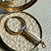 18k gold quizzing glass magnifying glass pendant on a textured light gray background
