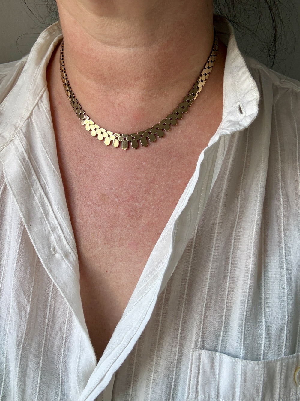 Person wearing a gold necklace with a white shirt