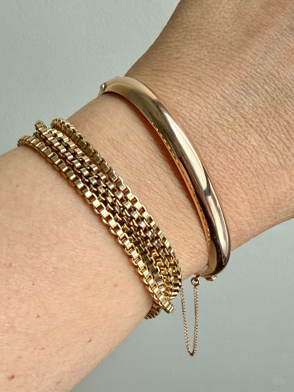 Gold bracelets on a wrist against a neutral background