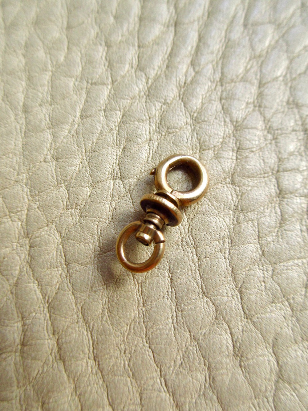 A small 14k gold antique swivel clasp placed on a textured off-white leather surface.