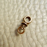 A small 14k gold antique swivel clasp placed on a textured off-white leather surface.
