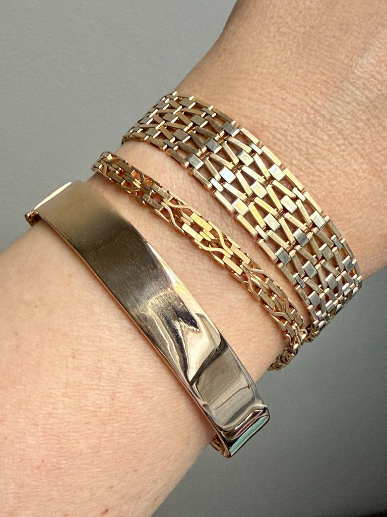Close-up of a wrist wearing multiple gold bracelets on a gray background