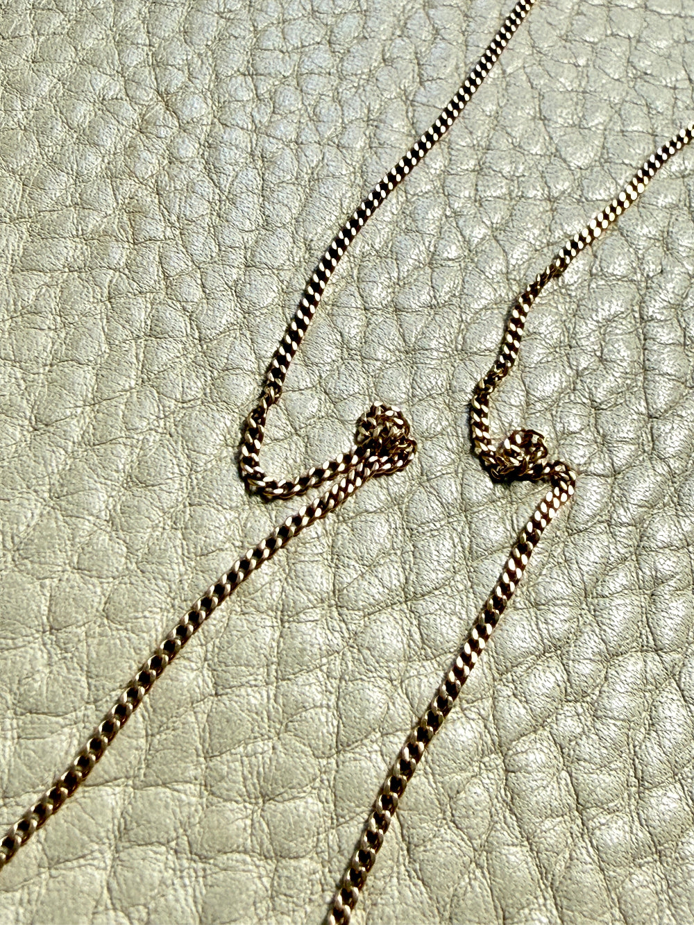 Gold chain necklace on a textured beige surface