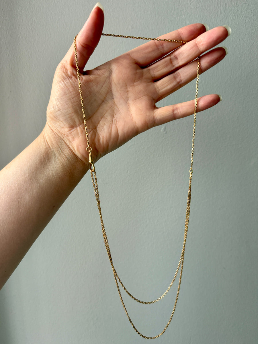 Gold chain necklace held by a hand against a plain background