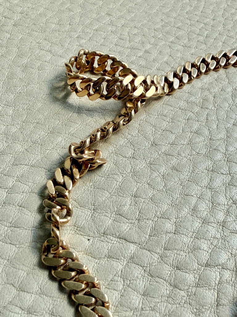 Gold chain on a textured light gray background. PenelopePenelope.com