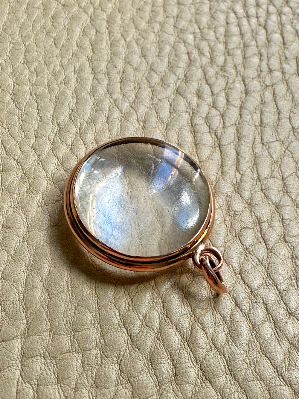 Clear glass antique pendant locket with gold setting on a textured beige surface