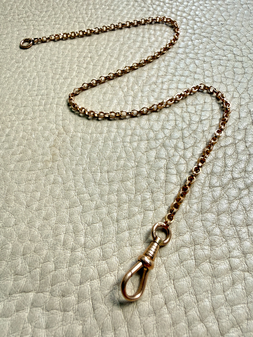 antique 18k Gold watch chain with dog clip on a textured light gray background