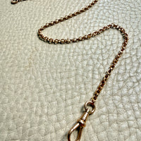 antique 18k Gold watch chain with dog clip on a textured light gray background