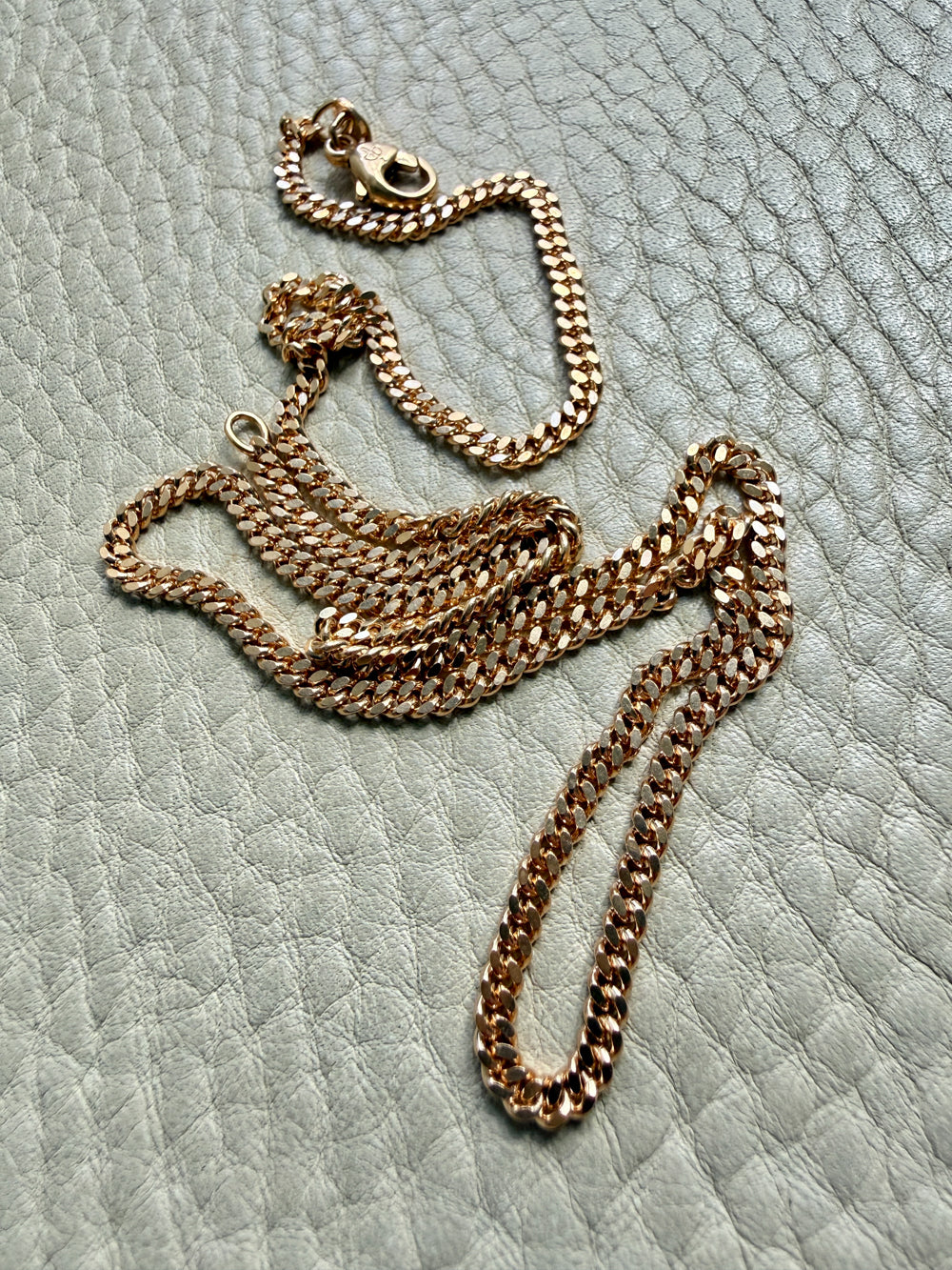 18k Gold curb chain necklace on a textured light surface