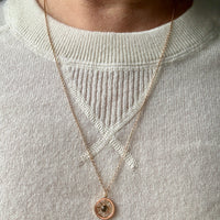 Necklace with a circular pendant worn by a person in a light gray sweater.