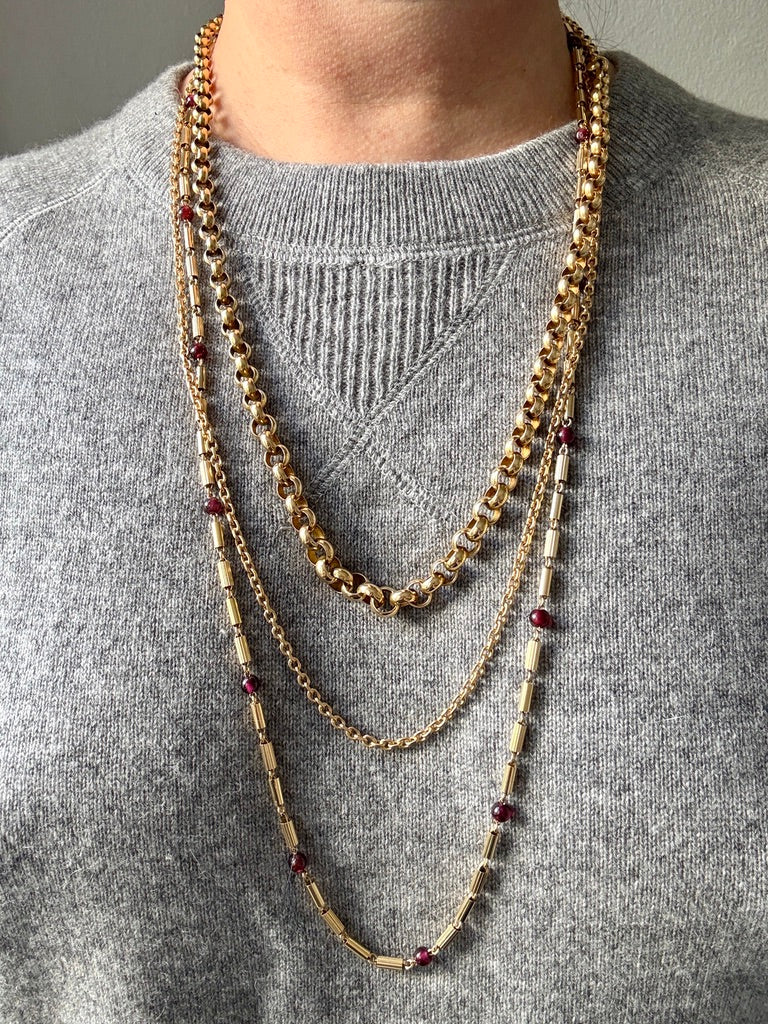 18k Gold chain necklaces with red garnets worn by a person on a gray sweater.