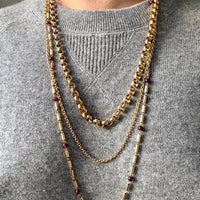 18k Gold chain necklaces with red garnets worn by a person on a gray sweater.