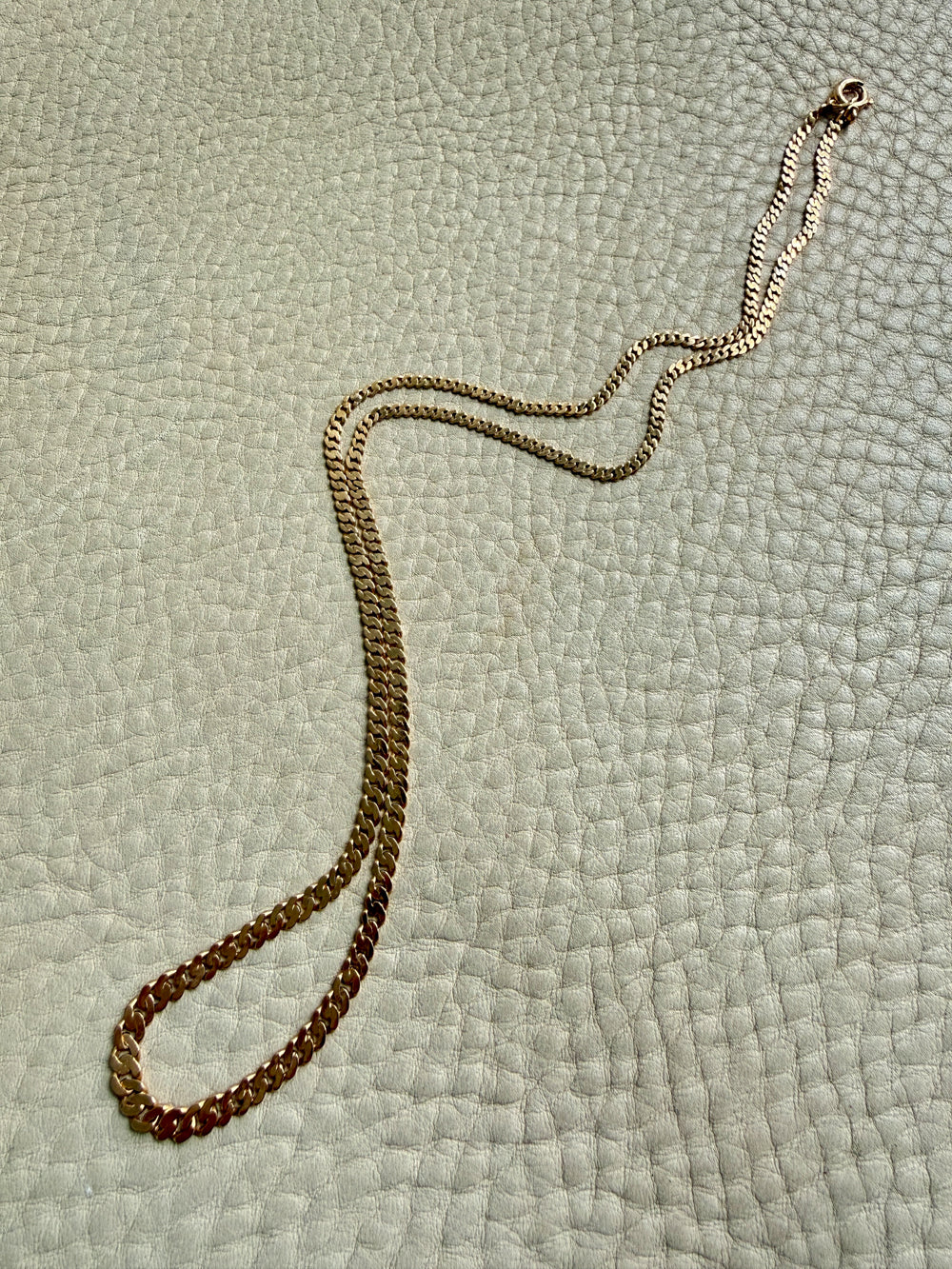 Gold chain necklace on a textured light green surface