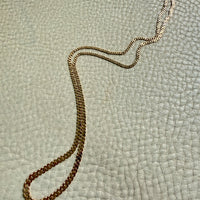 Gold chain necklace on a textured light green surface