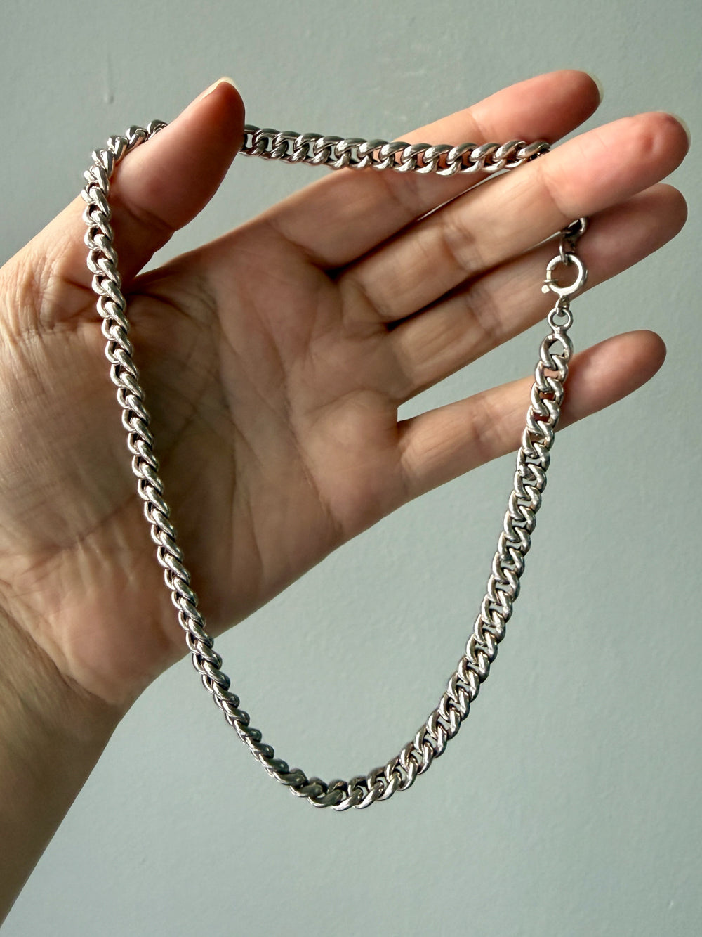 Hand holding a silver curb chain against a plain background