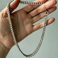 Hand holding a silver curb chain against a plain background