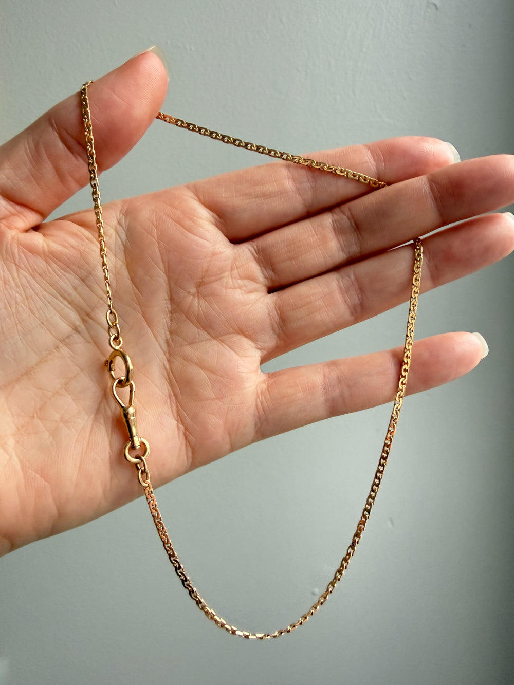Gold chain held by a hand against a gray background