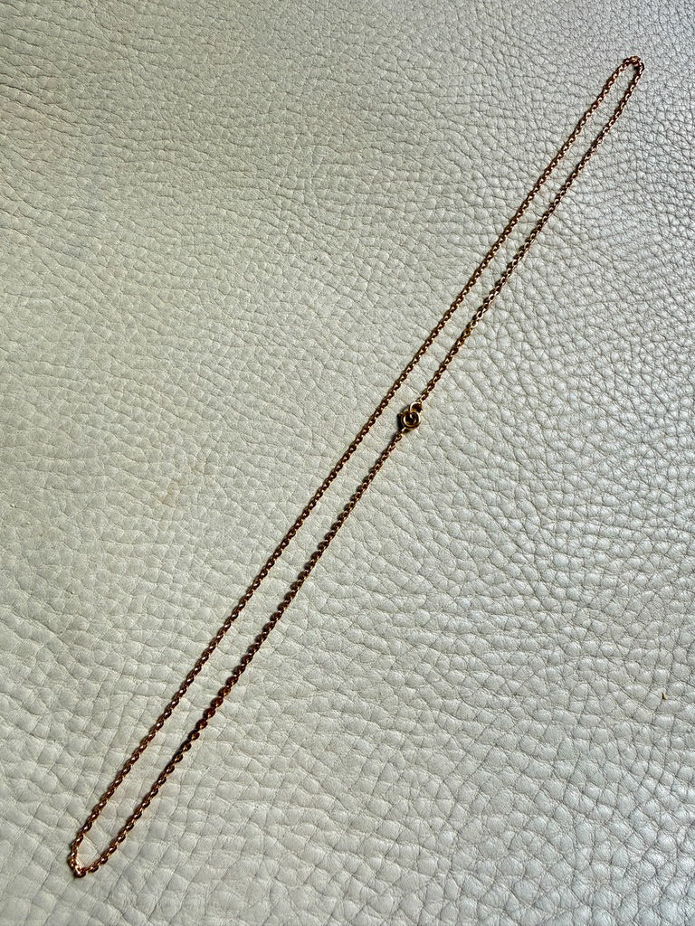 Gold chain necklace on a textured beige surface