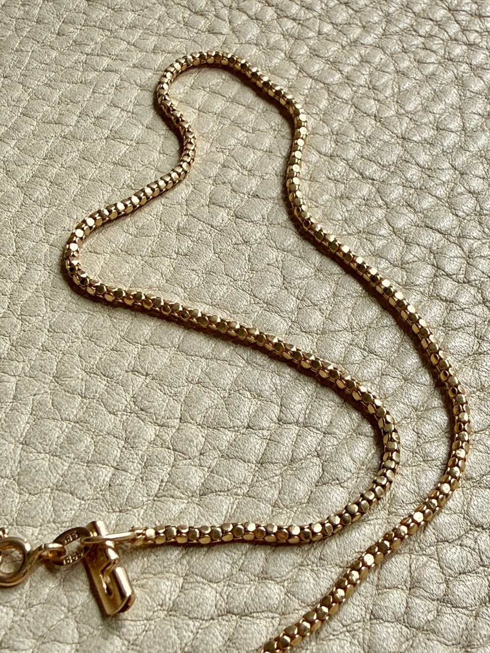 Gold chain necklace on a textured beige surface