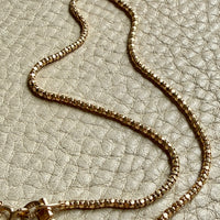 Gold chain necklace on a textured beige surface