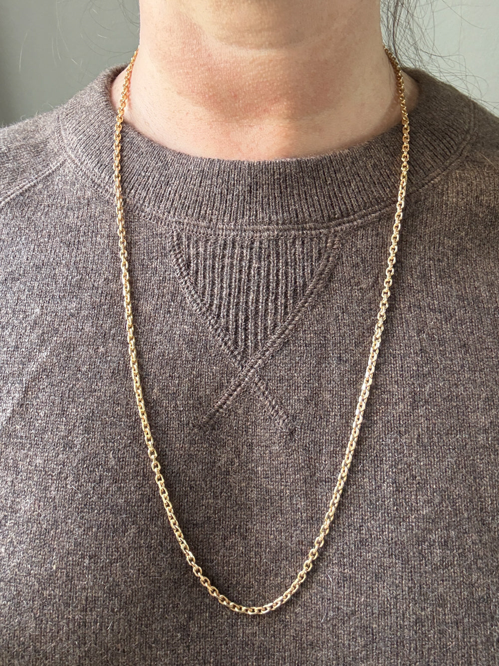 Gold chain necklace on a person wearing a gray sweater.