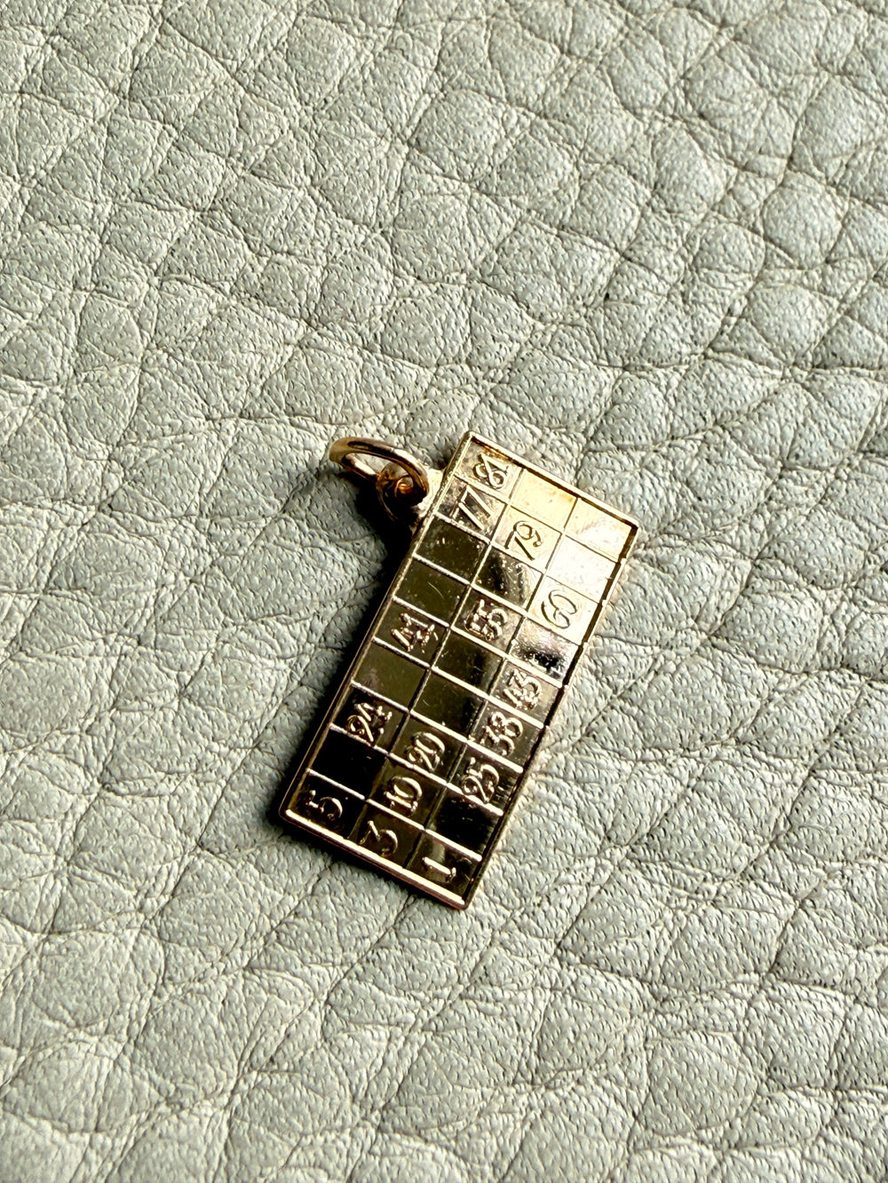 18k Gold British bingo board pendant with raised characters on a textured light gray background