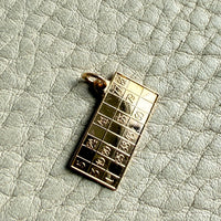 18k Gold British bingo board pendant with raised characters on a textured light gray background