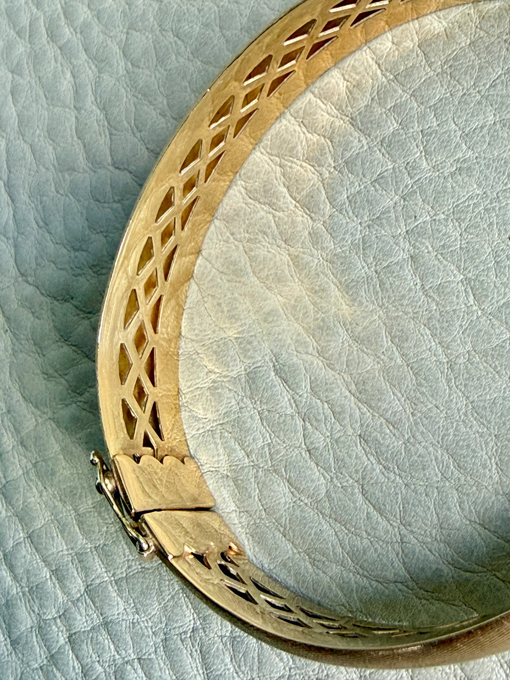 Gold bracelet with intricate design on a textured light blue background
