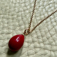 red purpurin egg pendant on a gold chain against a textured light green background