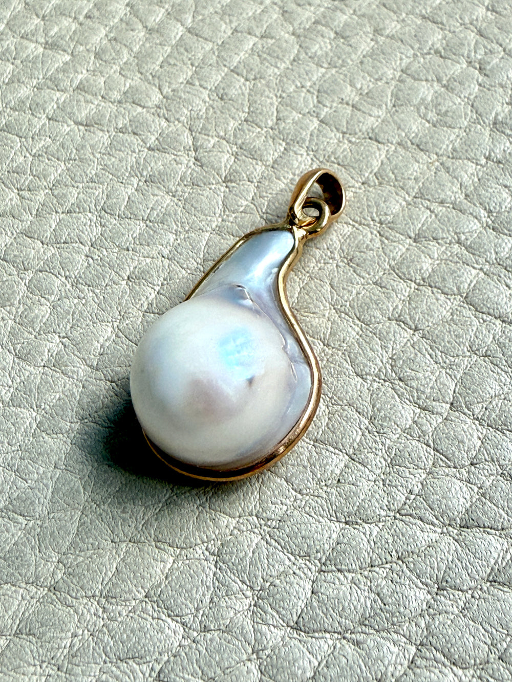 Pearl pendant with gold setting on a textured light gray background