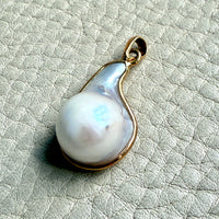 Pearl pendant with gold setting on a textured light gray background