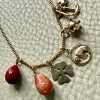 Necklace with various charms including a red bead, anchor, clover, and others on a textured light green background.