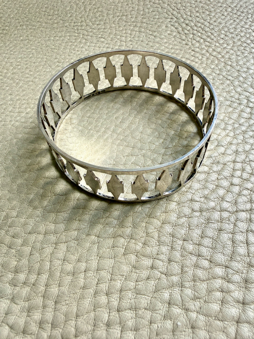 Decorative silver bangle bracelet with cutout pattern on a textured surface