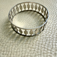Decorative silver bangle bracelet with cutout pattern on a textured surface