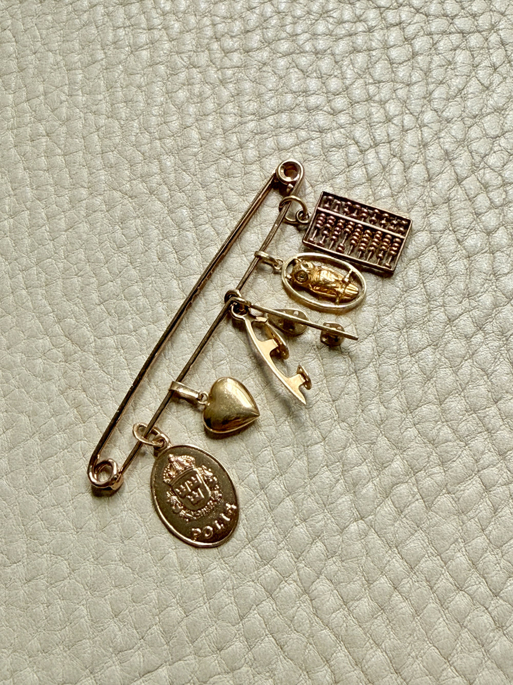 Gold brooch with various charms on a textured light background. PenelopePenelope.com
