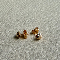 Pair of gold stud earrings on a light gray textured surface