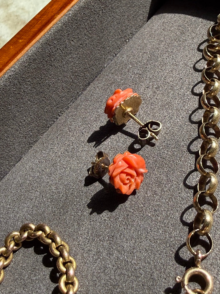 Pair of coral rose earrings on a gray surface with gold chains.