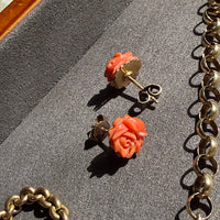 Pair of coral rose earrings on a gray surface with gold chains.