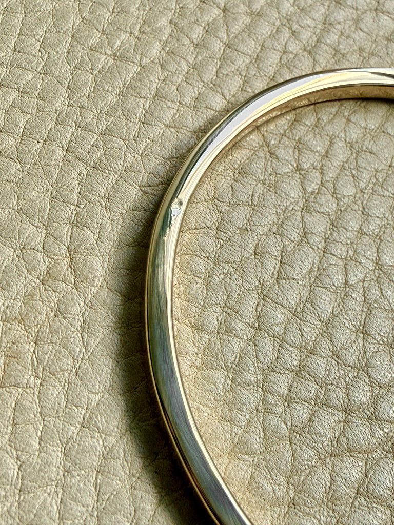 14k Gold solid round bangle on a beige textured surface