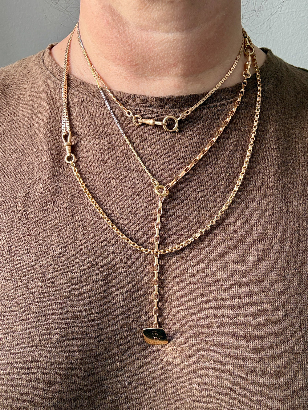 Person wearing multiple gold necklaces with pendants on a plain background
