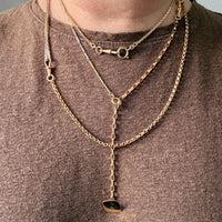 Person wearing multiple gold necklaces with pendants on a plain background