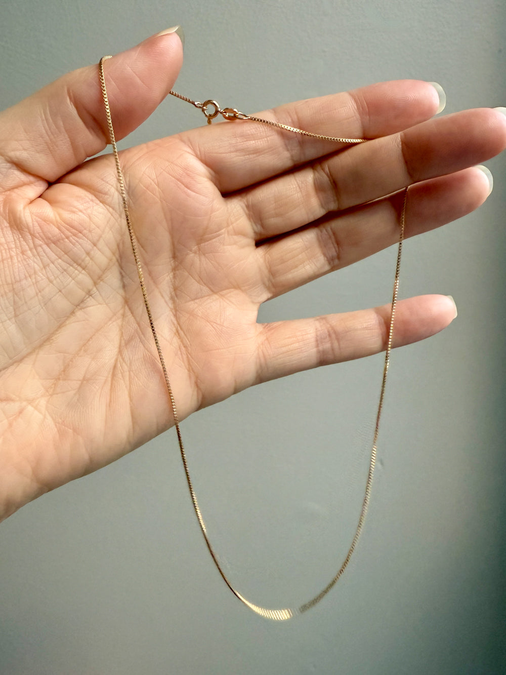 Gold chain held by a hand against a neutral background