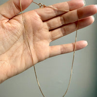 Gold chain held by a hand against a neutral background
