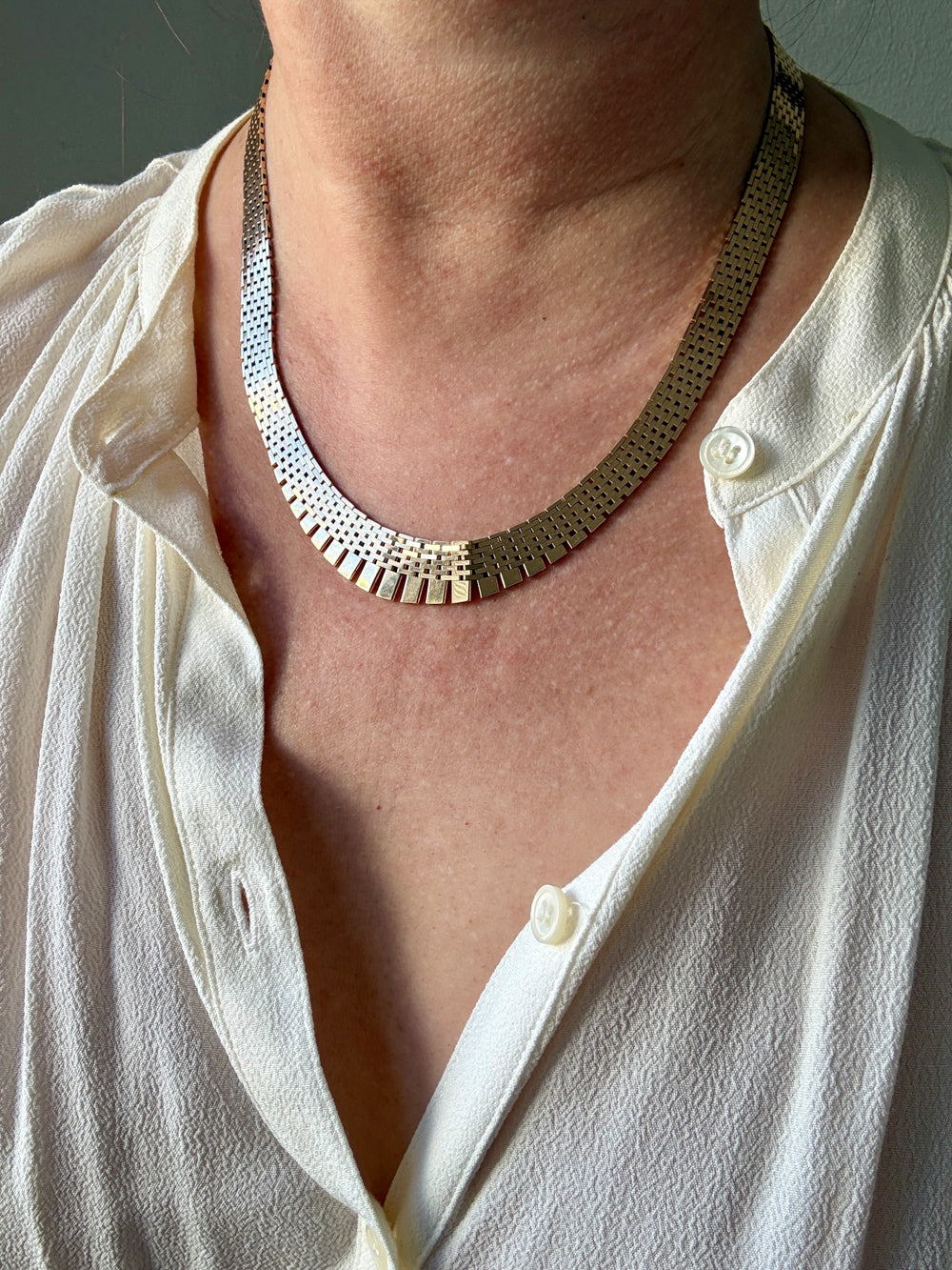 Close-up of a person wearing a gold necklace with a white shirt.
